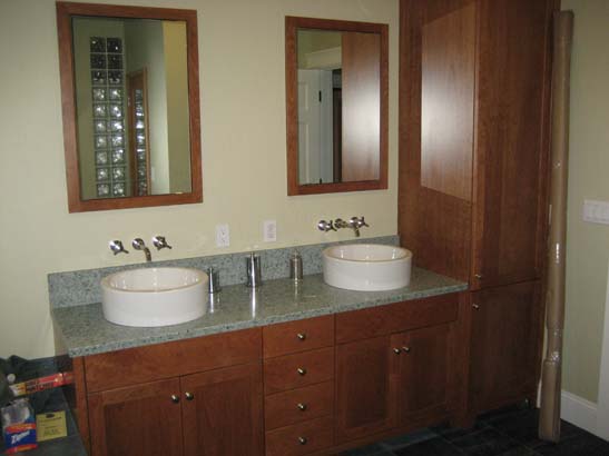 Ceramic bowl sinks on a green with black flecked granite counter top, all on cherrywood cabinets