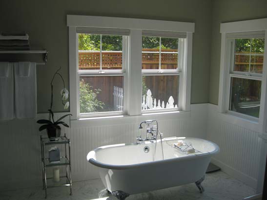 Different angle of a standalone bathtub with vintage stainless steel fixtures on a standard white lenolium tile floor