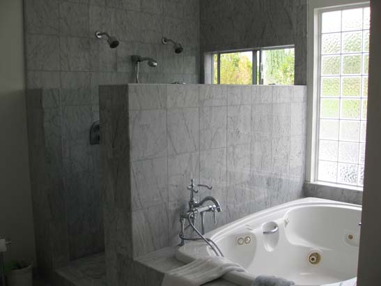 Gray tile privacy wall next to a white jaccuzi with stainles steel fixtures