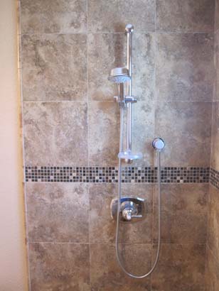 Tan tile shower with a black mosaic tile line in the center