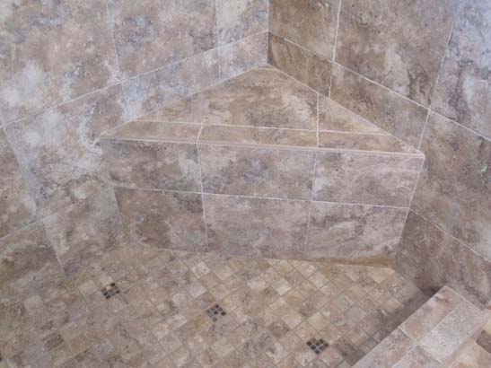 Different angle Tan tile shower with a black mosaic tile line in the center with stainless steel fixtures