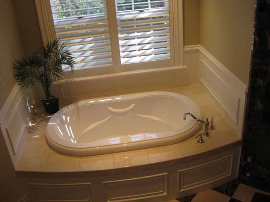 Closer angle of inset bathtub below a double window with vintage fixtures